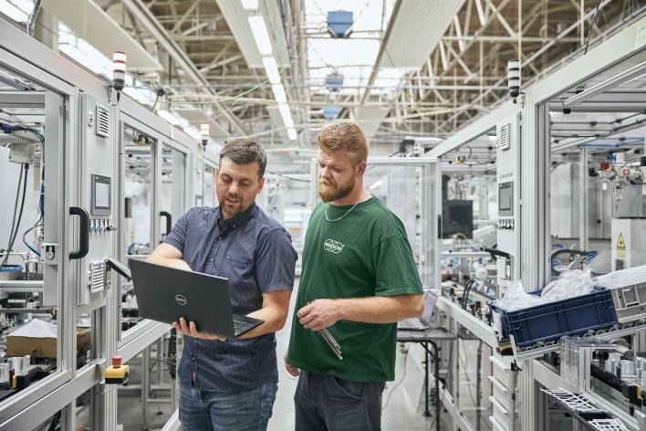 Zwei Mitarbeiter schauen zusammen auf einen Laptopn in der Produktionshalle